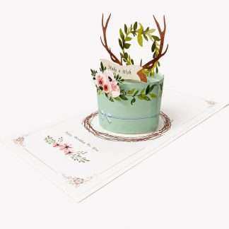 3D pop-up birthday card featuring brown antlers, a green leaf wreath, and pink flowers on a mint green base with a "Make a Wish" banner